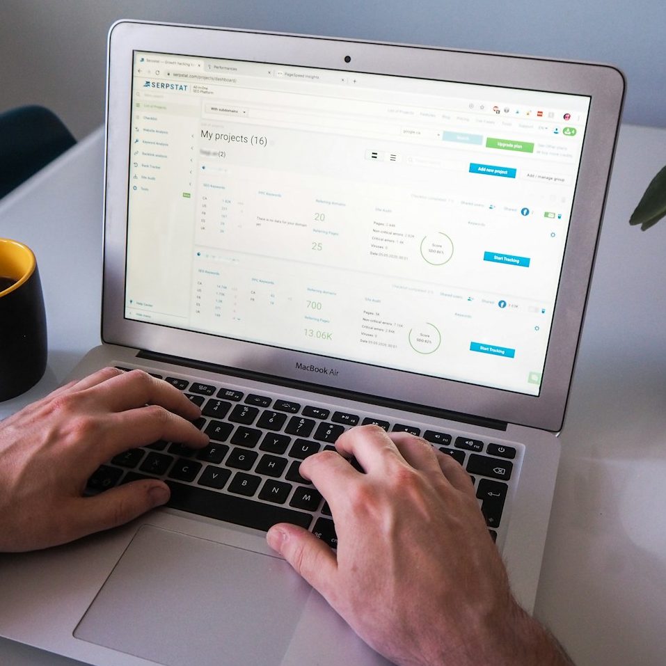 Eine Person tippt auf einem Laptop,- während ein Kaffeebecher daneben steht.